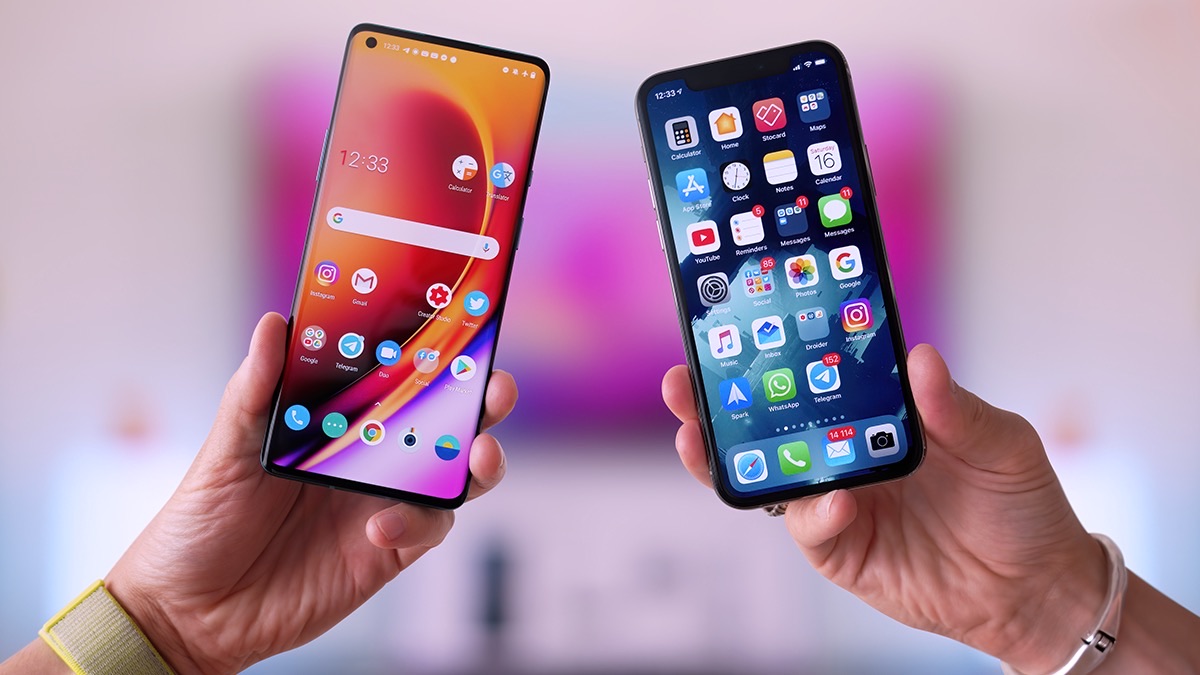Duas mãos segurando lado a lado um celular Android e um iPhone com as telas acesas