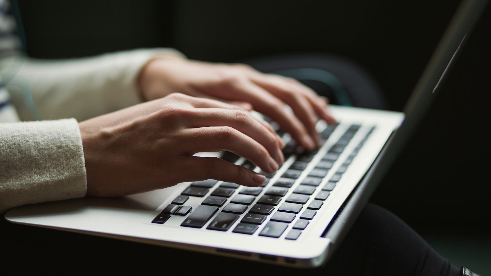 Mãos digitando em um notebook, em um ambiente com pouca luz
