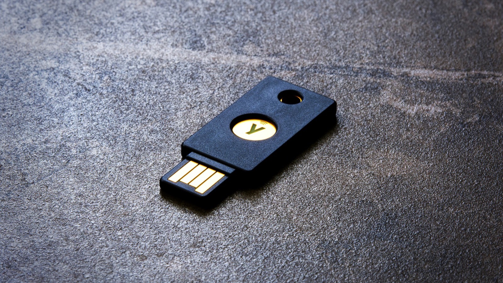 Chave de segurança física preta com conector USB sobre uma superfície de pedra escura