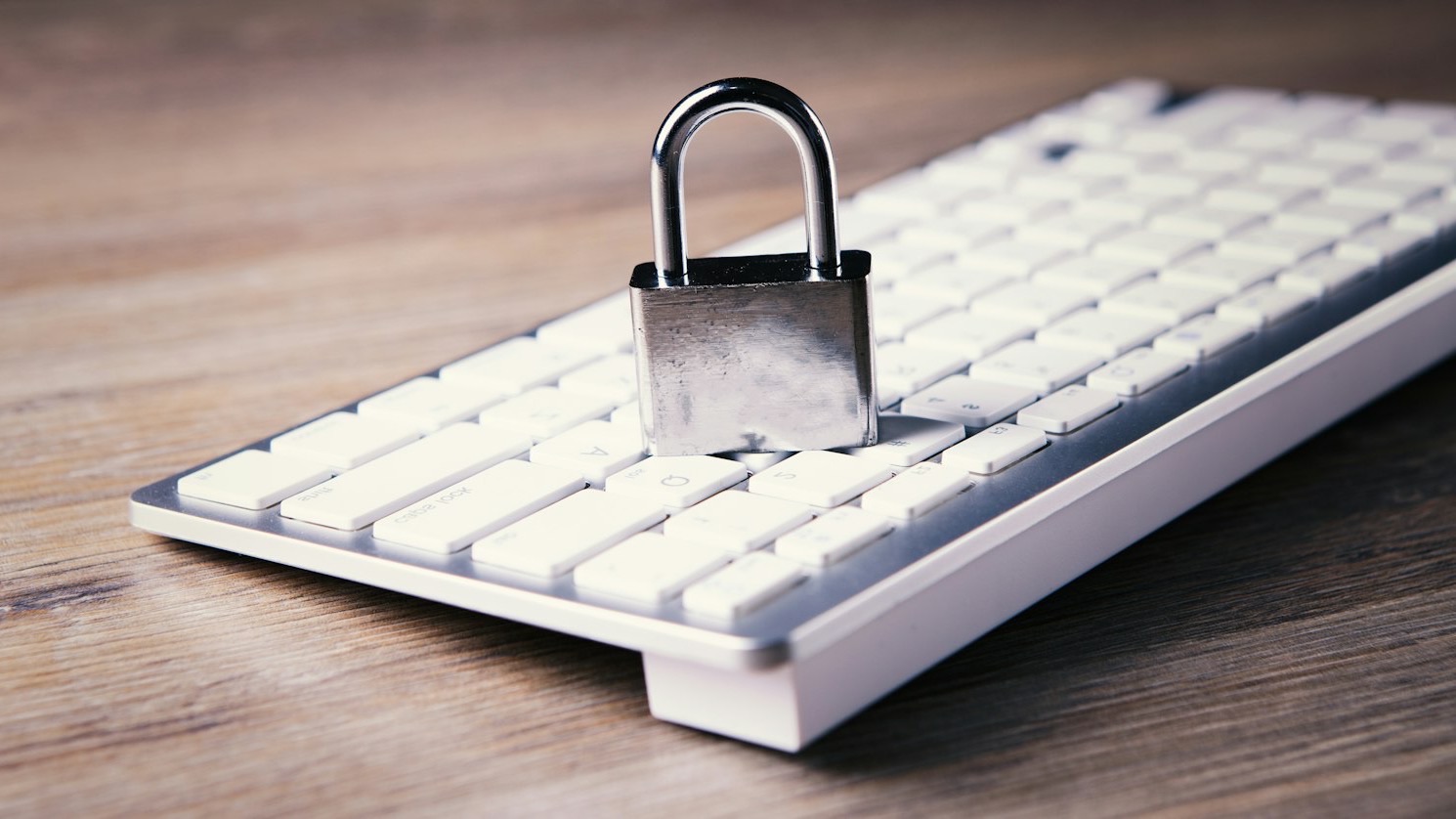 Cadeado de metal sobre um teclado branco de computador, em uma mesa de madeira