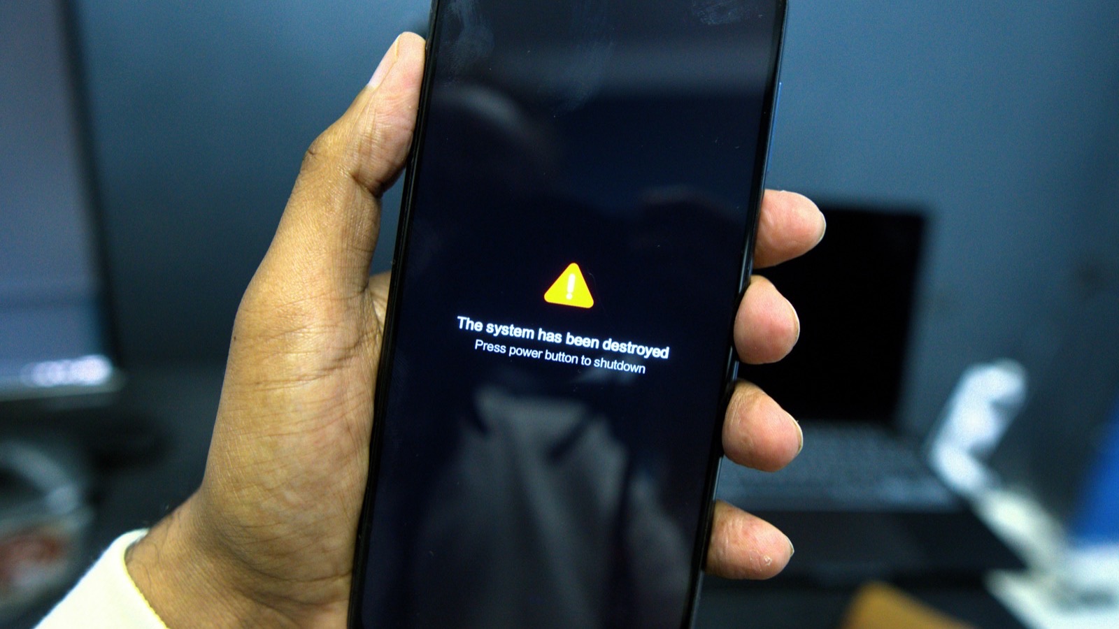 Mão segurando um celular preto com um triângulo amarelo de alerta na tela