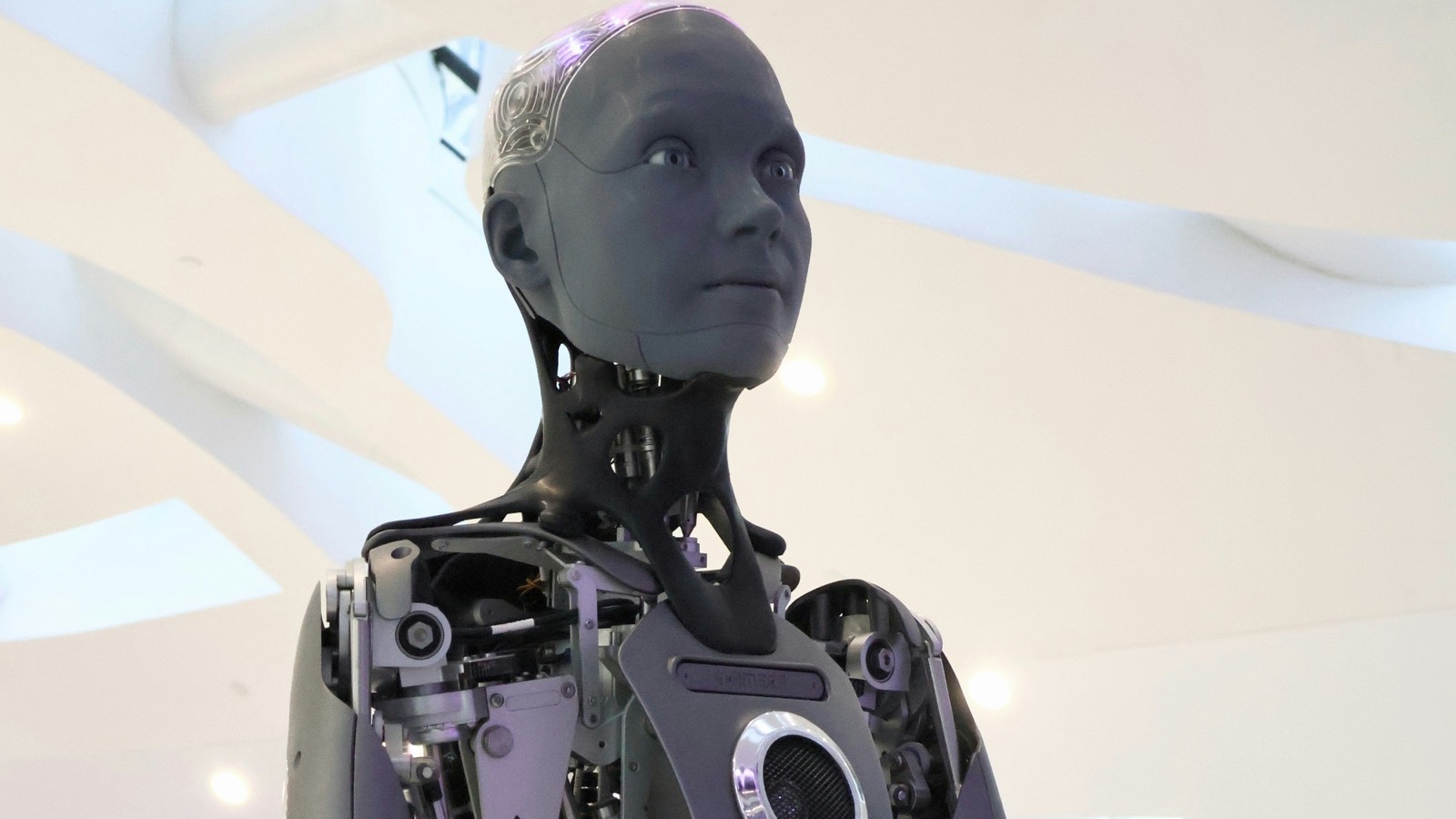 Robô humanoide de aparência humana, com o tronco e os braços mecânicos expostos, em um salão claro