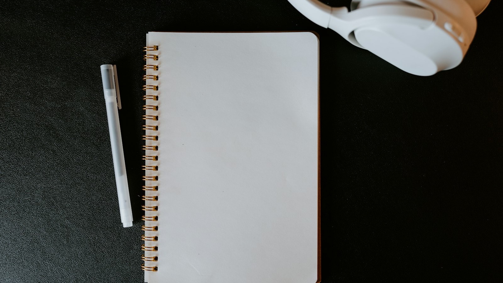 Caderno de espiral em branco com uma caneta e fones de ouvido brancos sobre uma mesa escura