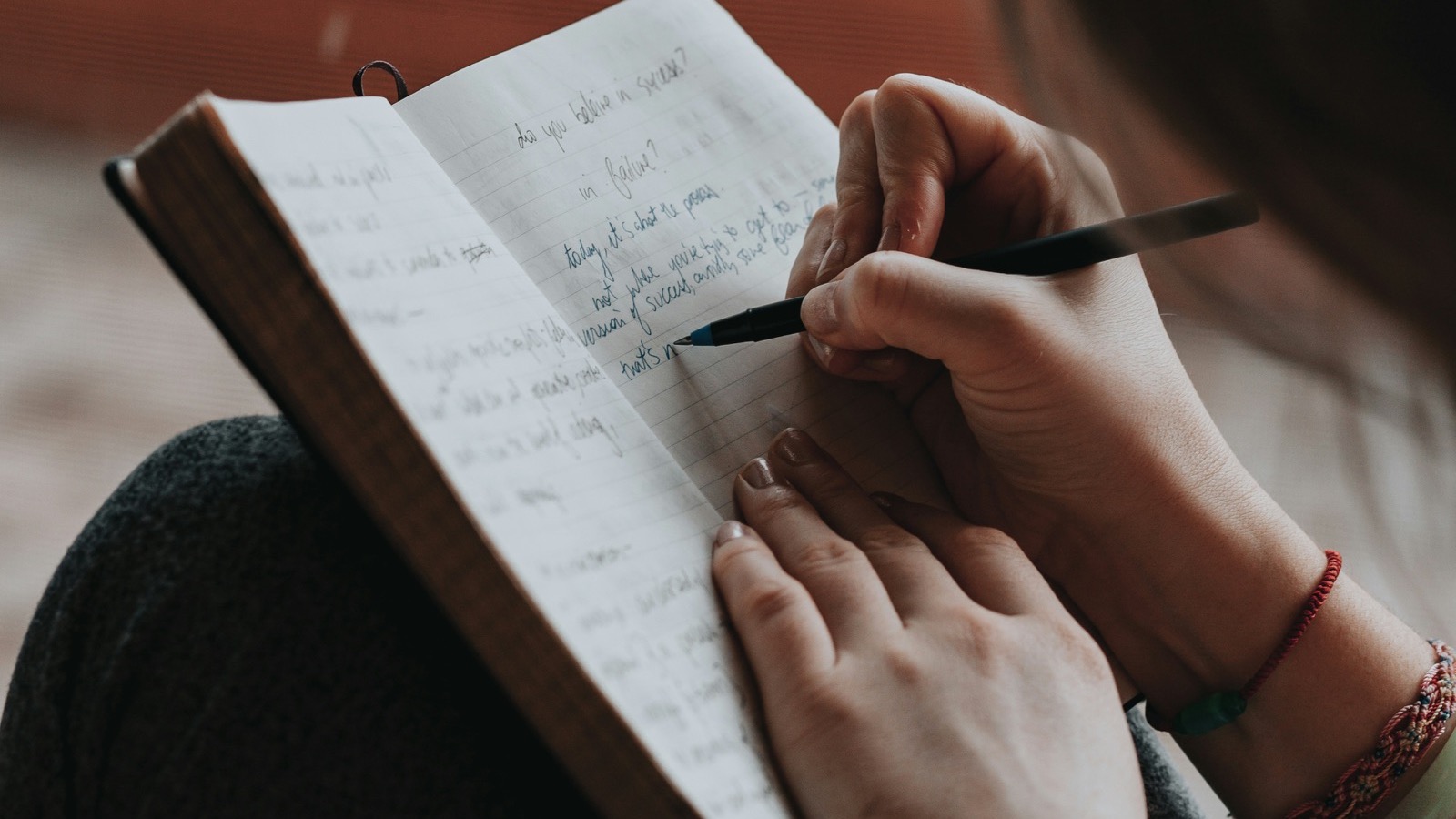 Mulher escrevendo à mão em um caderno aberto sobre o colo
