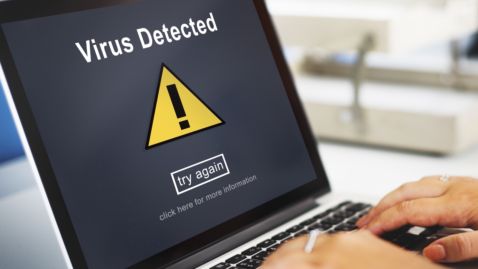 Notebook com alerta de vírus detectado na tela e mãos digitando no teclado