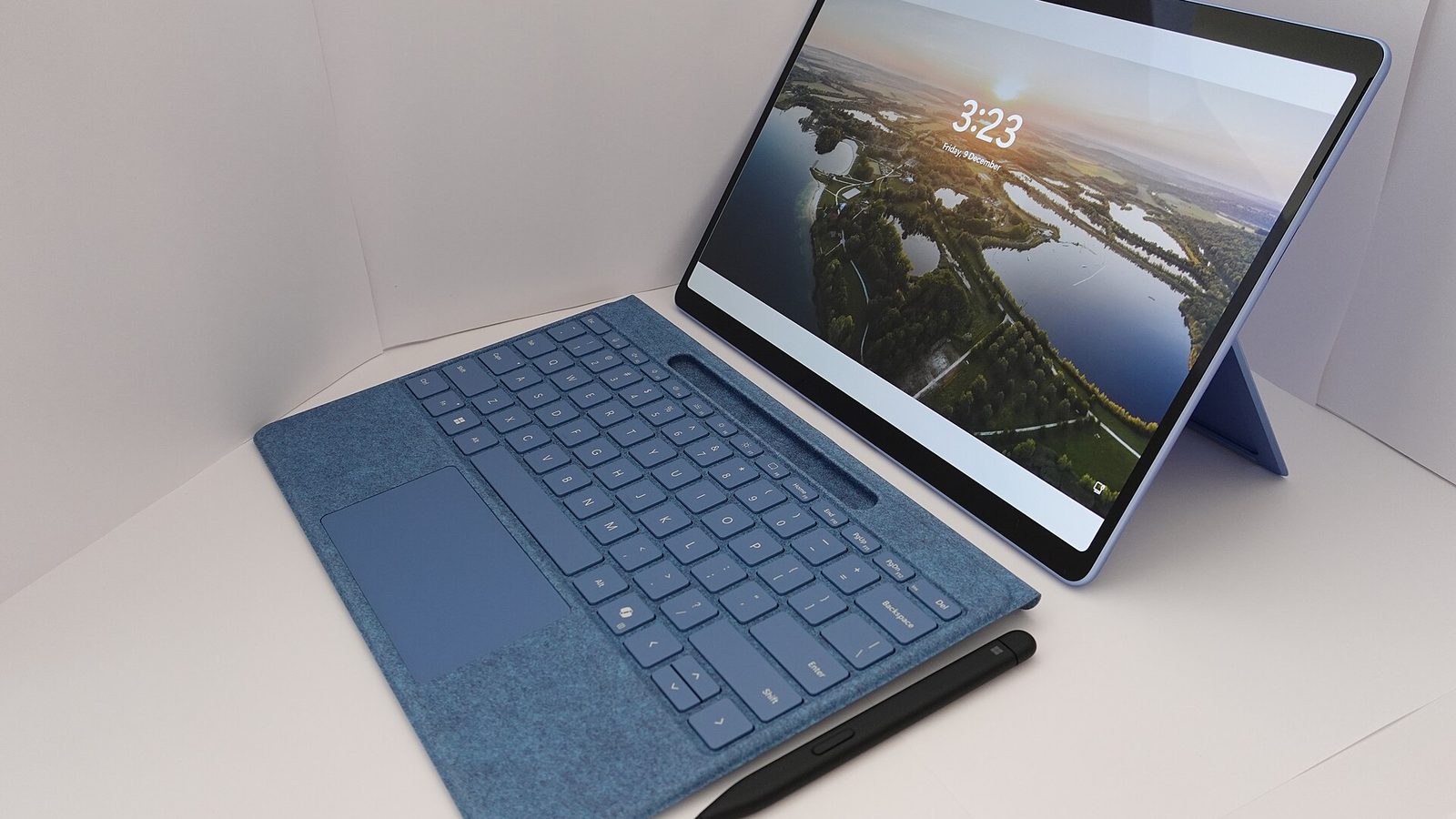 Notebook azul com a tela ligada e o teclado acoplado ao lado, sobre uma superfície branca
