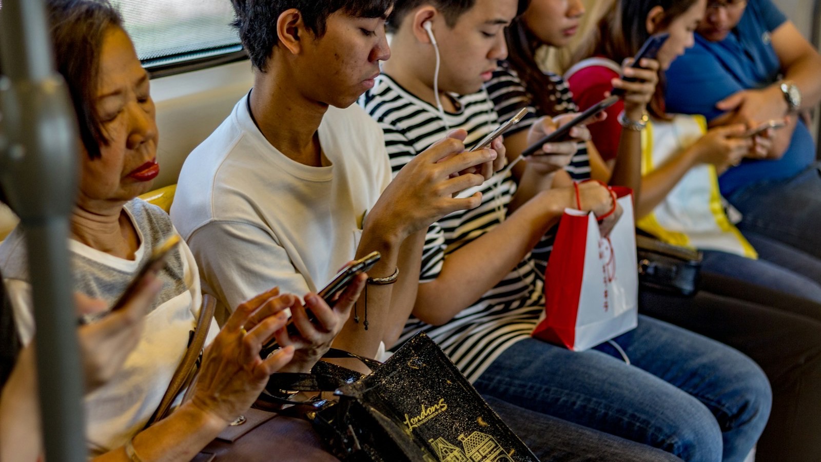 Passageiros sentados lado a lado em um trem, todos olhando para o celular