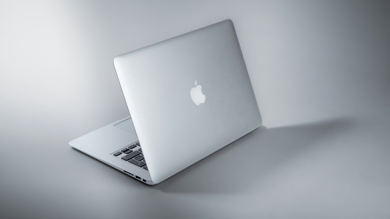 MacBook prateado aberto, visto de costas, sobre fundo cinza